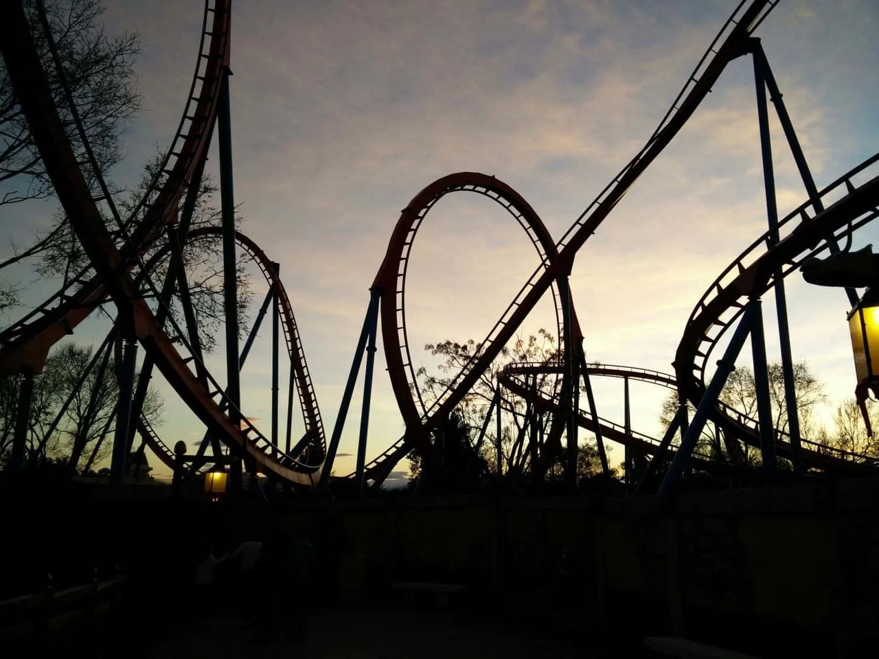 Montanha-russa em parque de diversões ao entardecer, com céu colorido ao fundo.