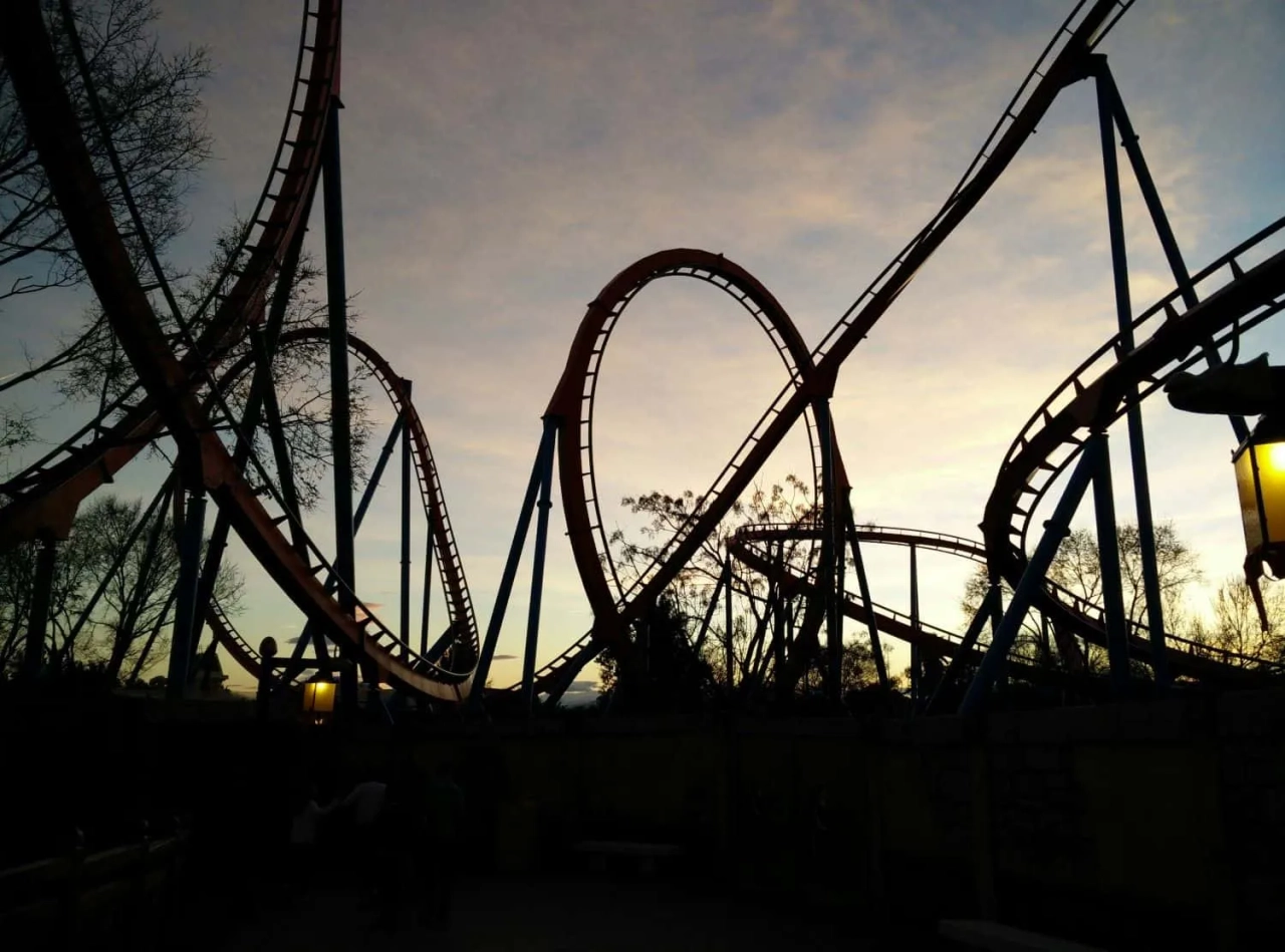 Montanha-russa em parque de diversões ao entardecer, com céu colorido ao fundo.