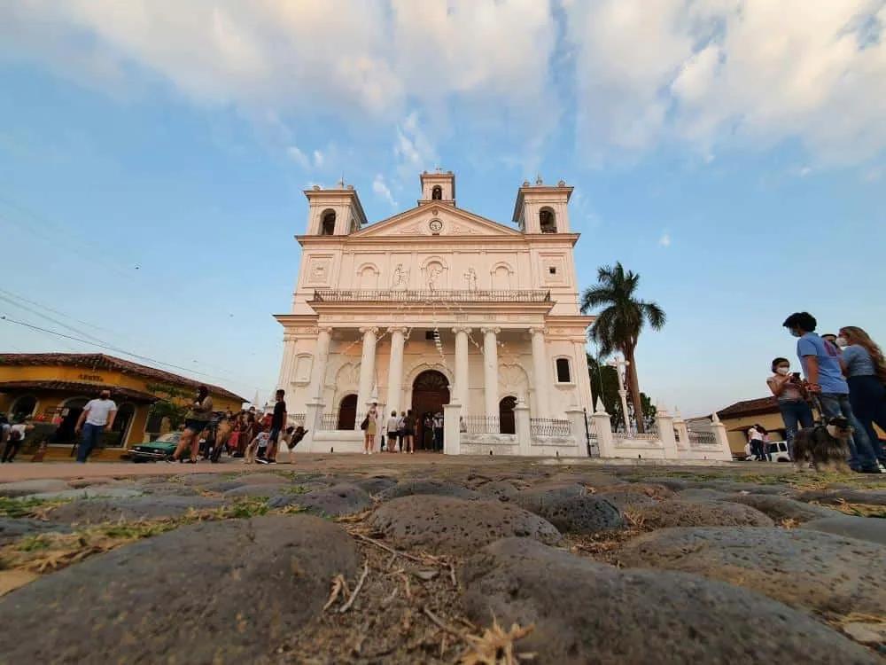 Iglesia blanca con columnas, rodeada de personas y un cielo azul al atardecer.