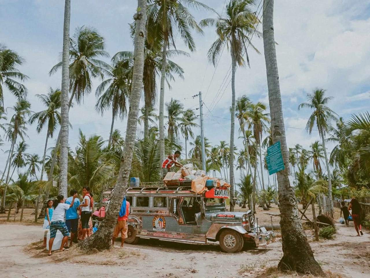 Grupo de personas junto a un jeepney en un paisaje tropical con palmeras.