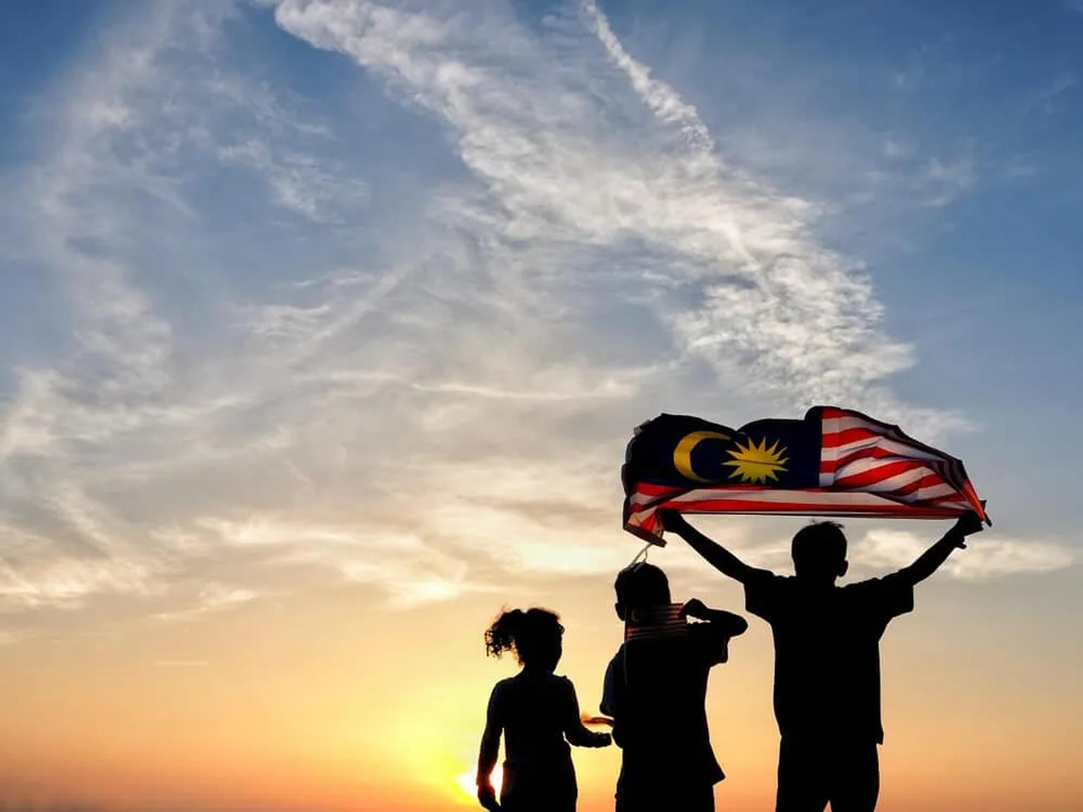 tres jovens seguram uma bandeira da malasia a contra luz