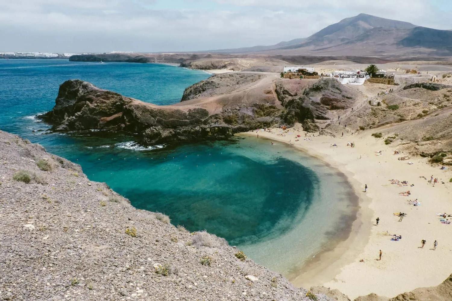 Praia com águas cristalinas e areia, cercada por montanhas nas Ilhas Canárias.