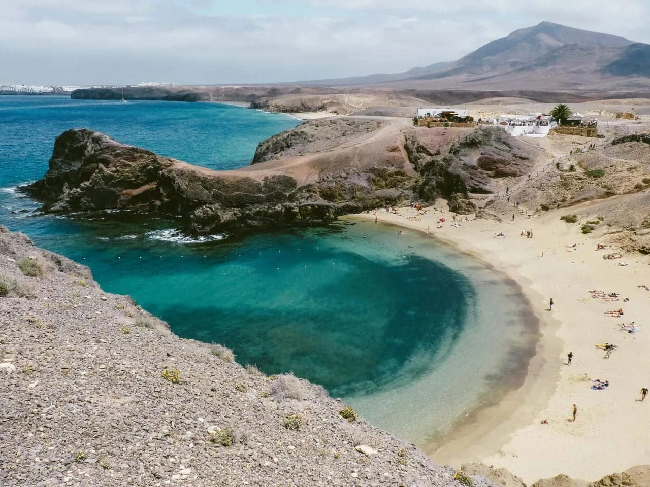 Praia com águas cristalinas e areia, cercada por montanhas nas Ilhas Canárias.