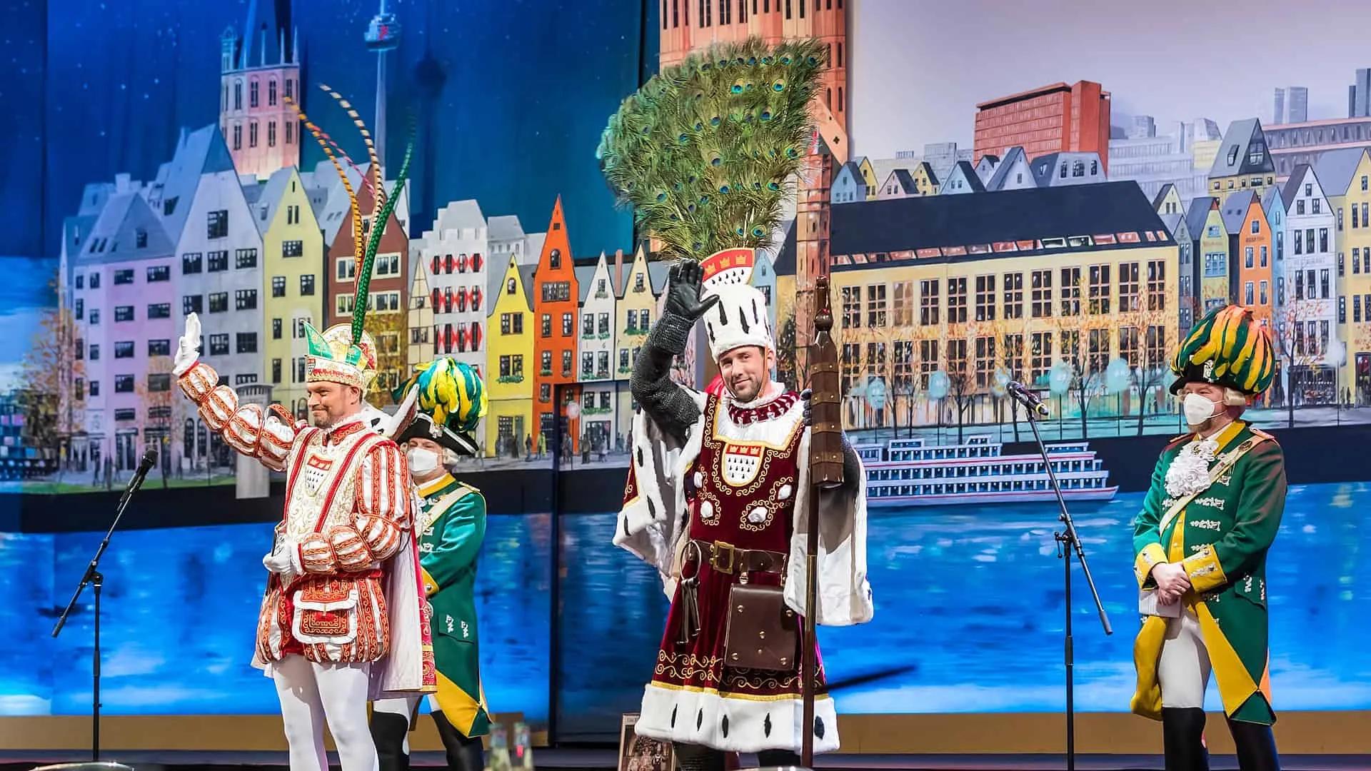 Três homens em trajes festivos em um palco, celebrando o Carnaval.