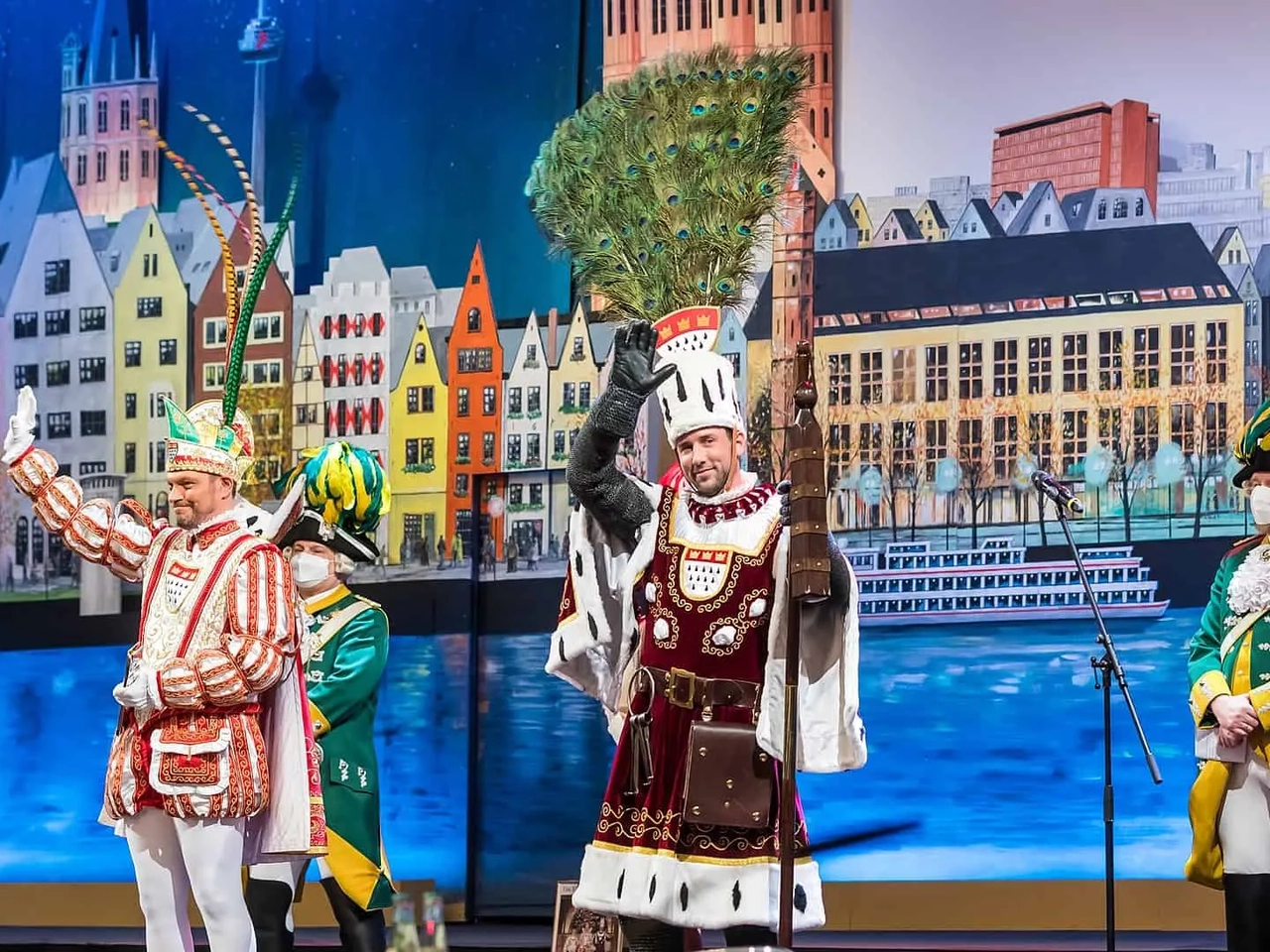 Três homens em trajes festivos em um palco, celebrando o Carnaval.