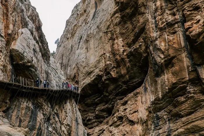 Sendero estrecho y elevado entre imponentes paredes de roca, con personas caminando.