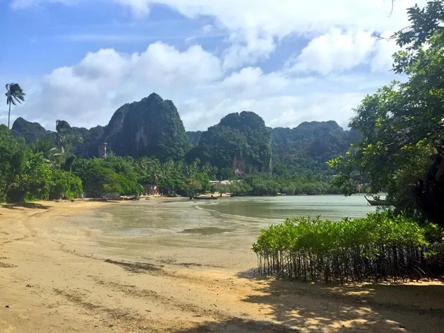 Playa con montañas y vegetación tropical en Tailandia. Cielo parcialmente nublado.