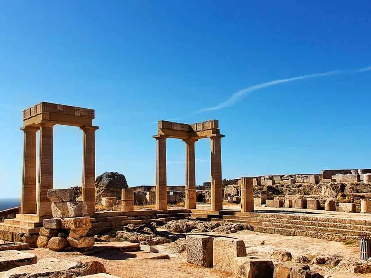 Ruínas de colunas antigas sob um céu azul, representando a história da Grécia.