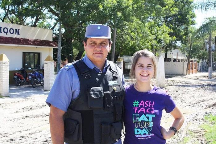 Un policía y una joven sonríen frente a un edificio en un entorno soleado.