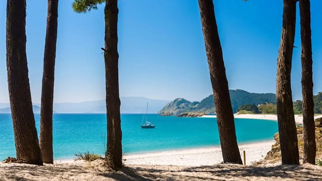Praia das Ilhas Cíes com águas cristalinas e vegetação ao fundo. Barco ancorado.