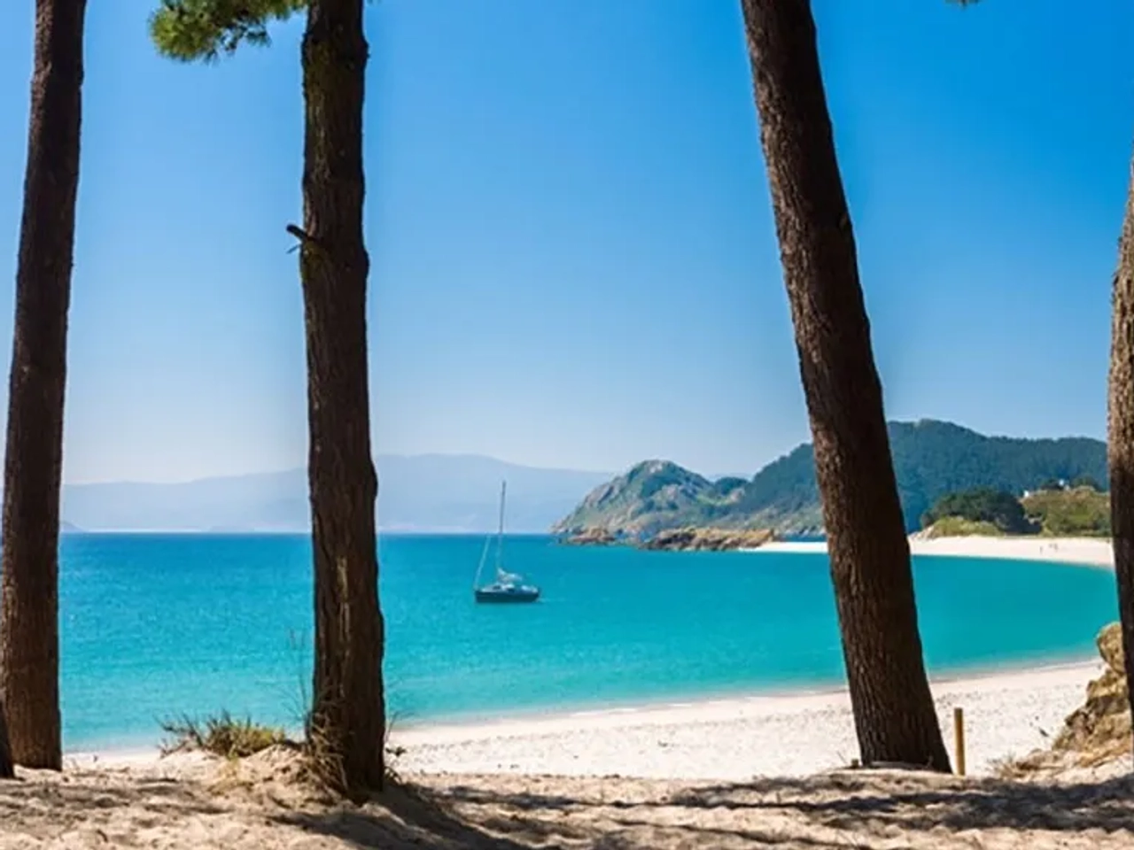 Praia das Ilhas Cíes com águas cristalinas e vegetação ao fundo. Barco ancorado.