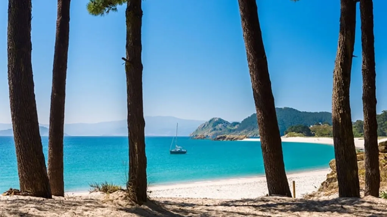 Praia das Ilhas Cíes com águas cristalinas e vegetação ao fundo. Barco ancorado.