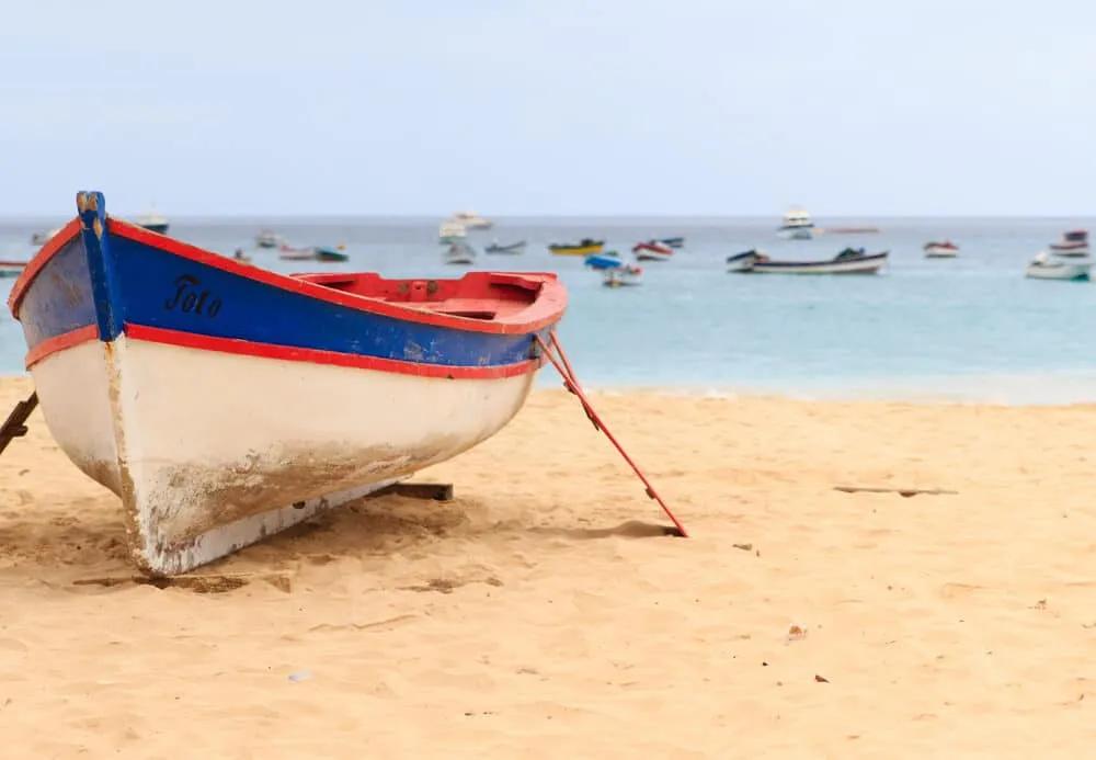 barco branco, azul e vermelho pousado no areal da praia de santa maria na ilha do sal em cabo verde