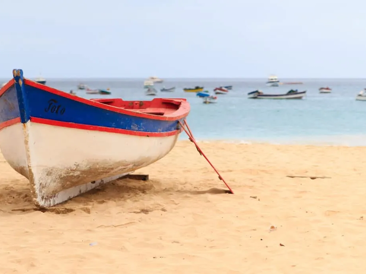 barco branco, azul e vermelho pousado no areal da praia de santa maria na ilha do sal em cabo verde