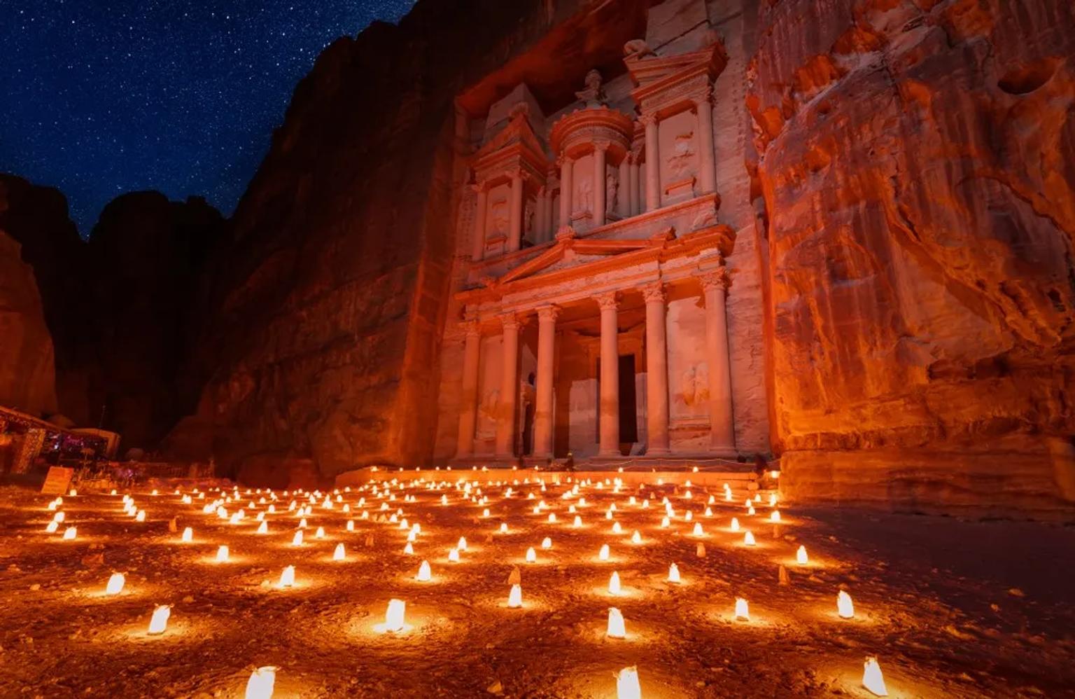 Petra iluminada por velas sob um céu estrelado, destacando sua arquitetura impressionante.