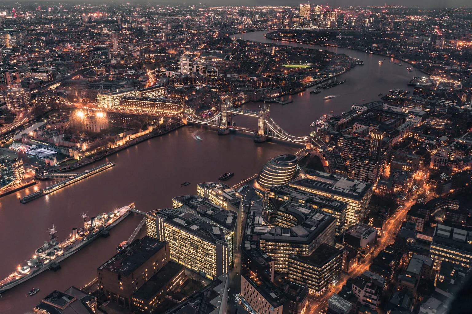 Aerial view of London at dusk, featuring the Thames River and Tower Bridge.