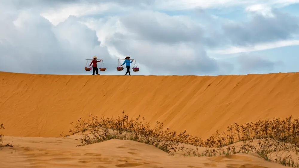 duas pessoas carregam bens pelas dunas de areia de mui ne