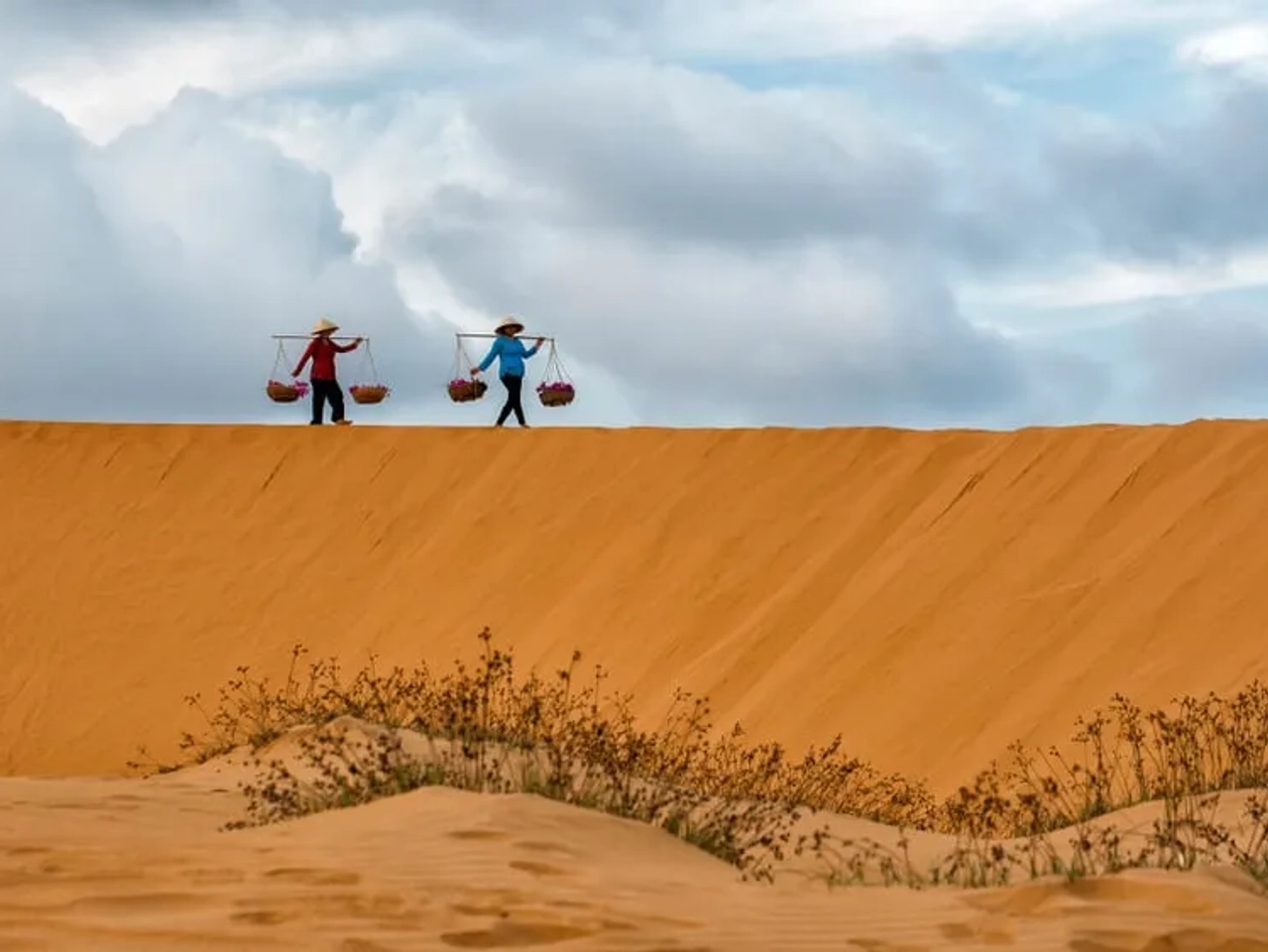 duas pessoas carregam bens pelas dunas de areia de mui ne