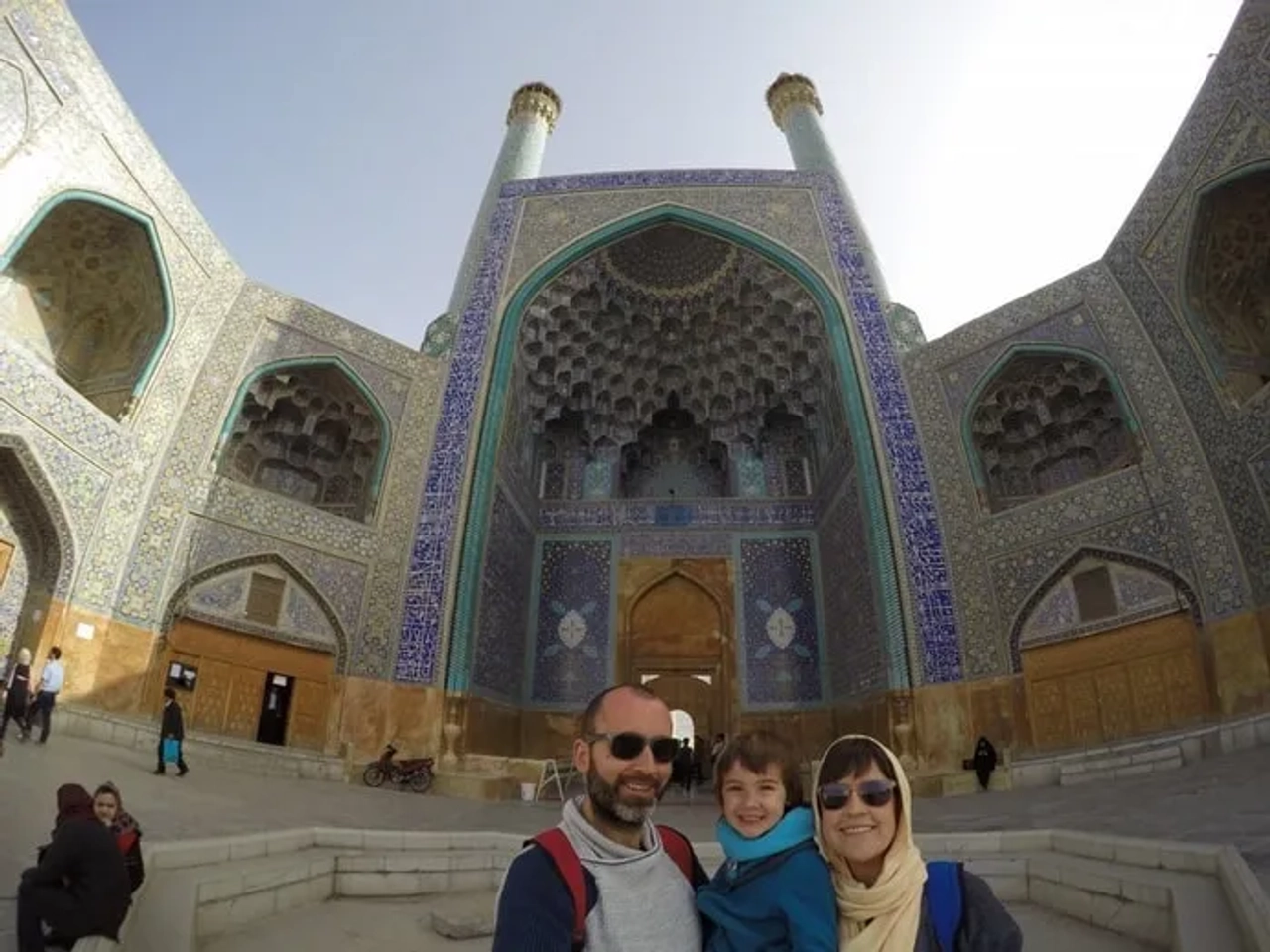 Familia sonriente frente a un majestuoso edificio con azulejos decorativos.