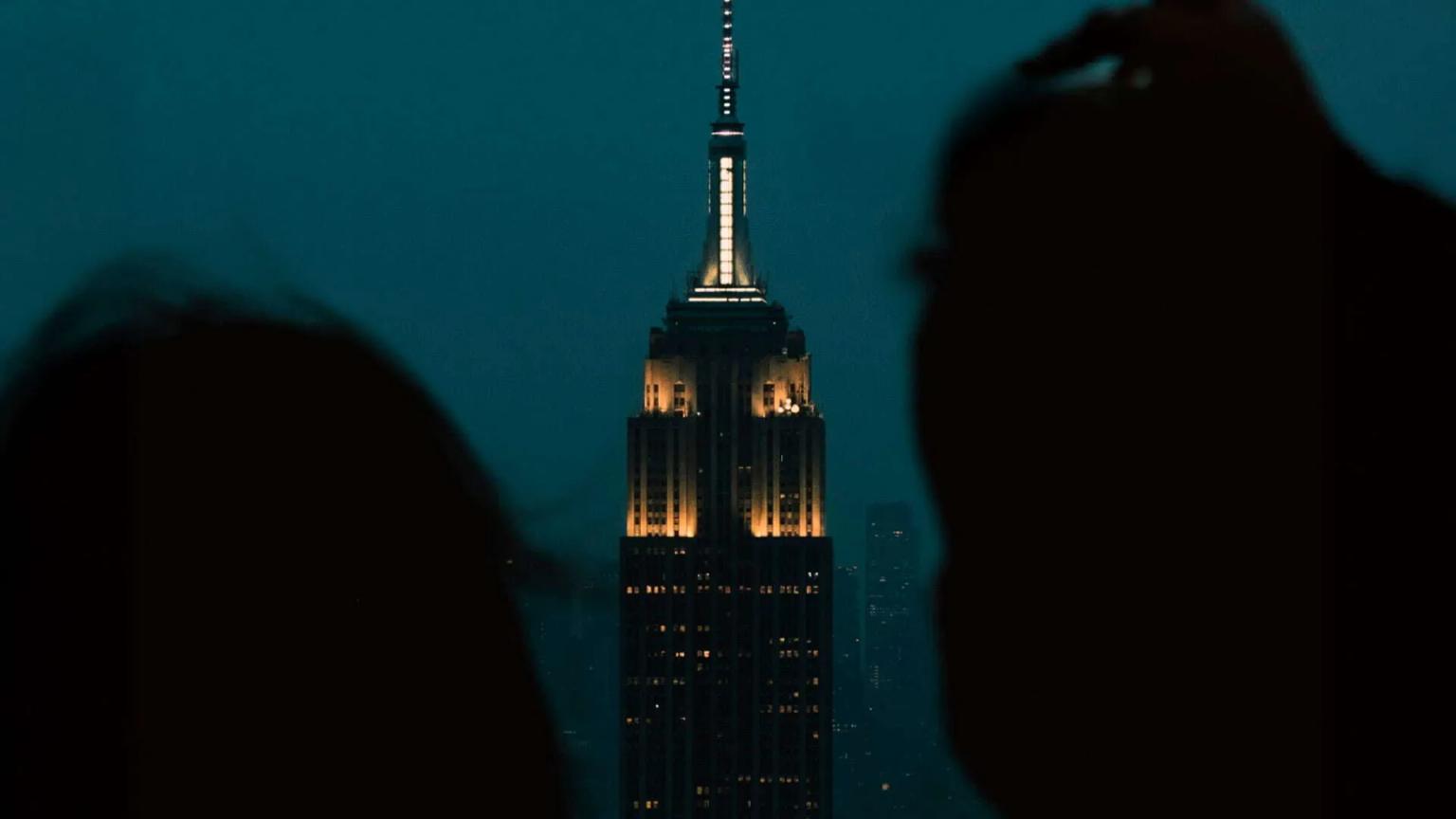 Silhuetas observando o Empire State Building iluminado à noite.