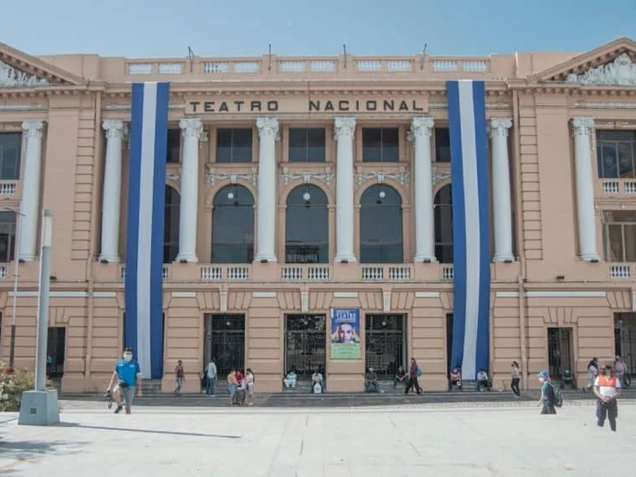 Teatro Nacional de El Salvador, edificio histórico con banderas y personas en la plaza.