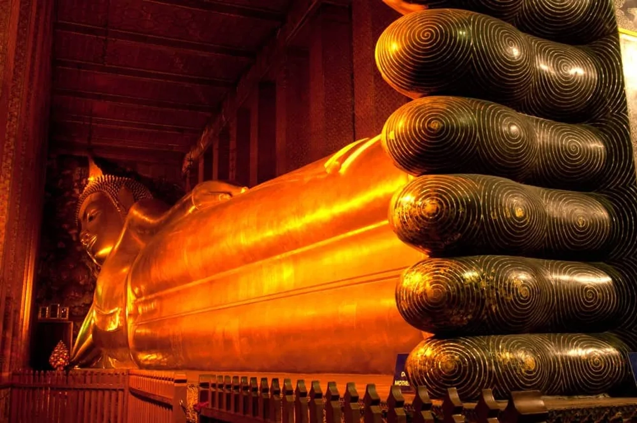 Statua dorata del Buddha disteso nel tempio Wat Pho di Bangkok, con i piedi decorati in primo piano.
