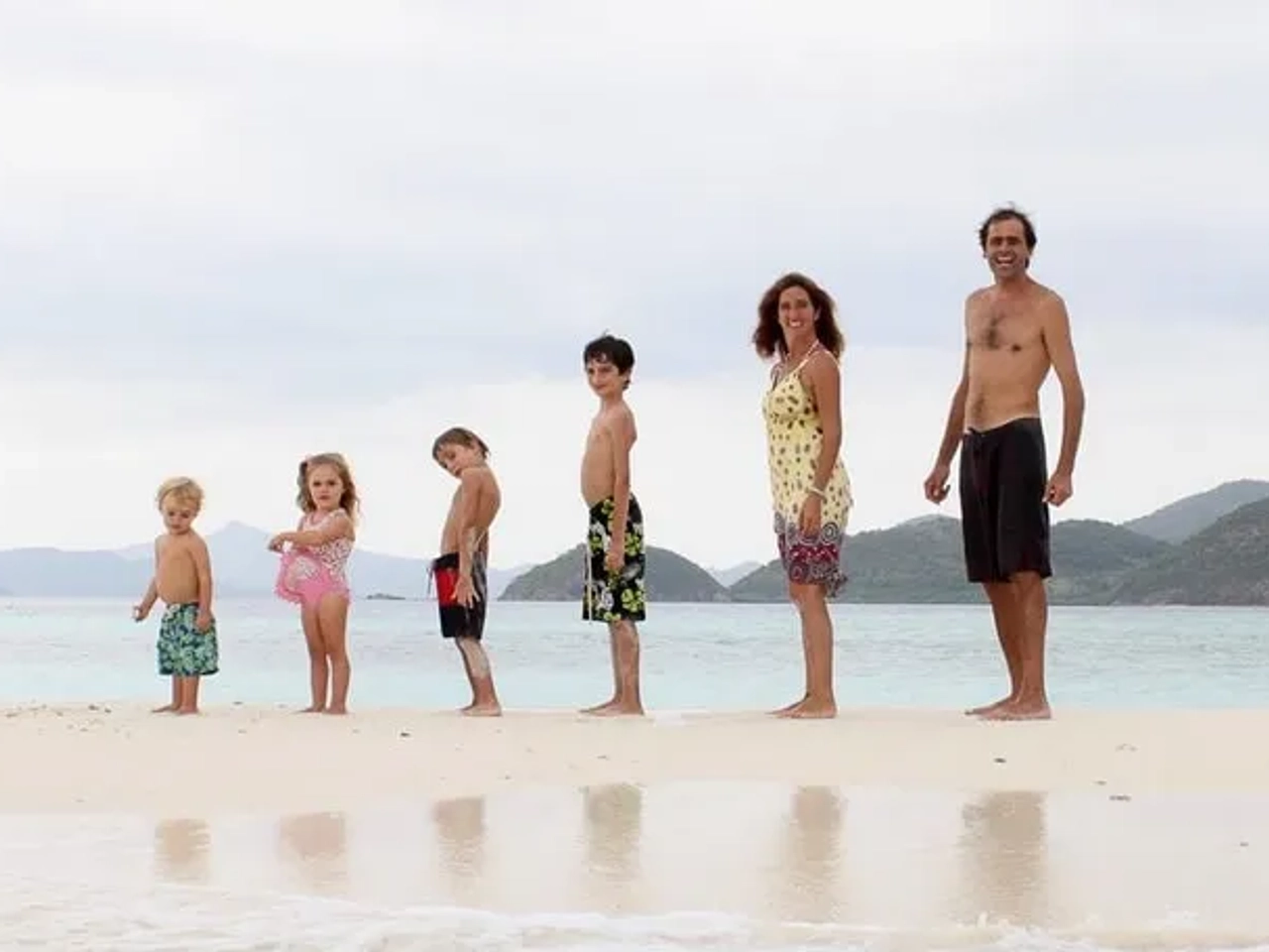 Familia de pie en la playa, disfrutando del mar y la arena.