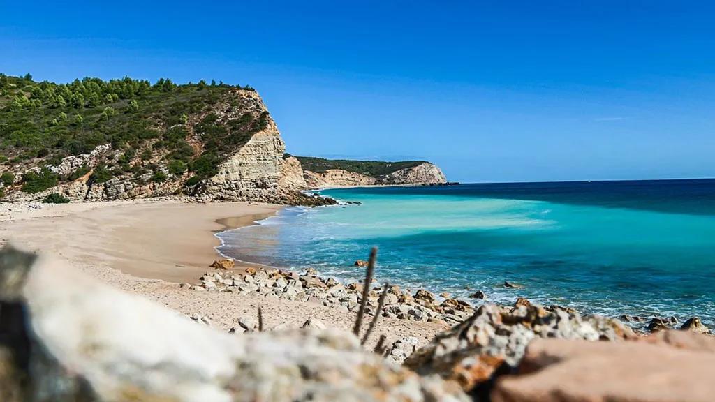Praia com águas cristalinas, cercada por falésias e vegetação verdejante.