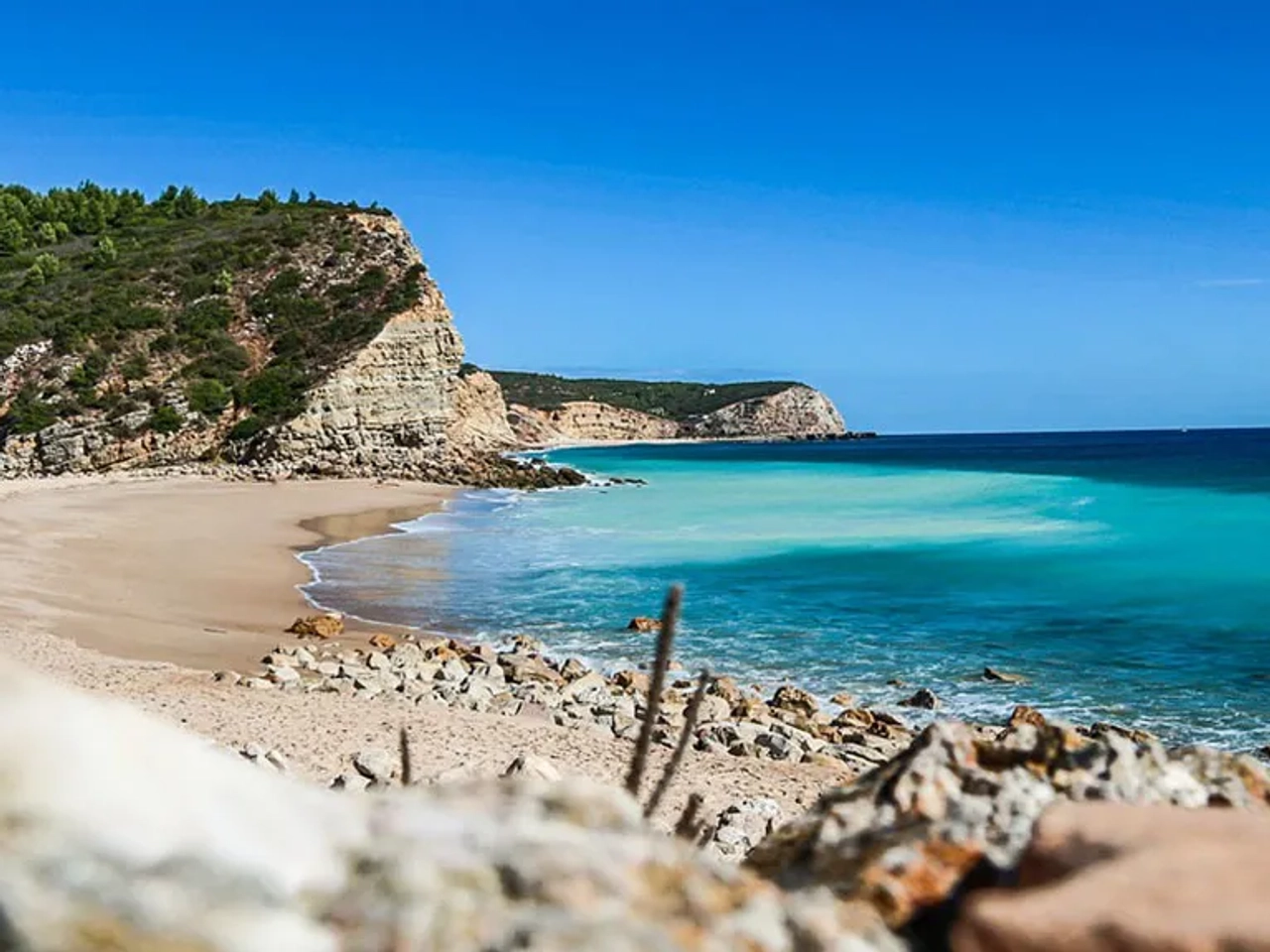 Praia com águas cristalinas, cercada por falésias e vegetação verdejante.