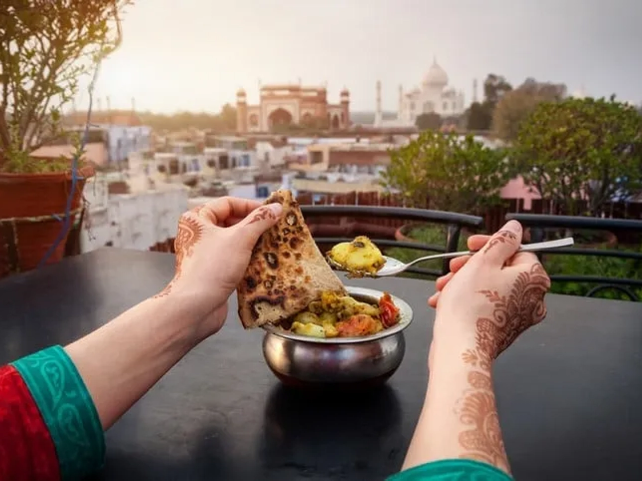 Manos sosteniendo comida típica con el Taj Mahal de fondo al atardecer.