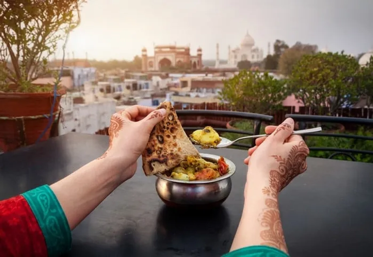 Manos sosteniendo comida típica con el Taj Mahal de fondo al atardecer.