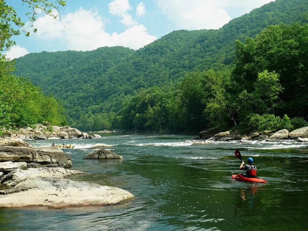 Pessoa praticando caiaque em um rio cercado por montanhas verdes.