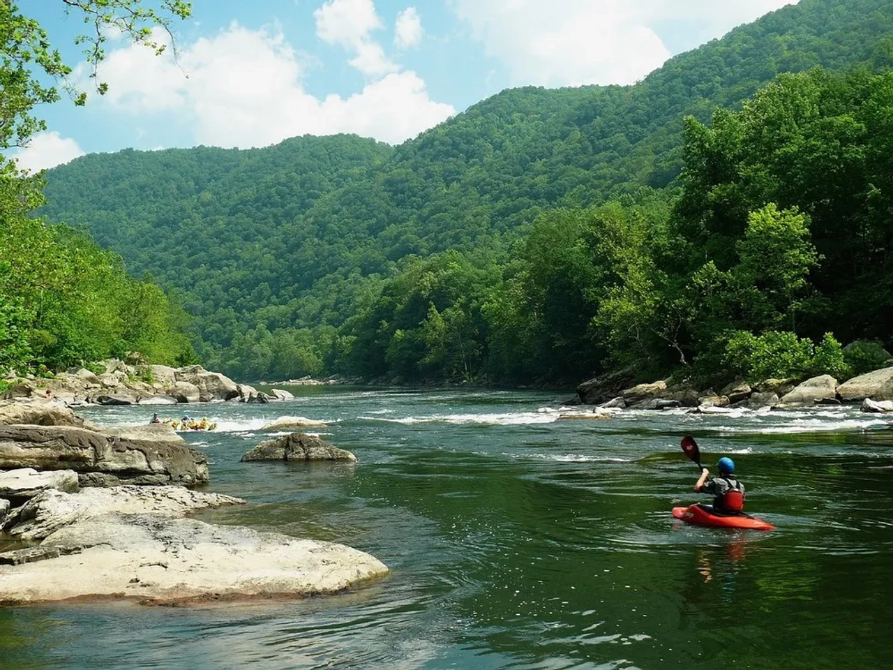 Pessoa praticando caiaque em um rio cercado por montanhas verdes.