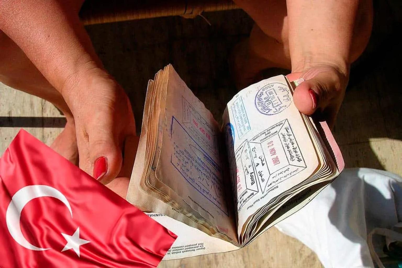 Pasaporte abierto con sellos y bandera de Turquía en el fondo.