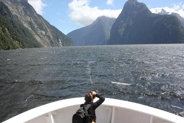 Persona en un barco observando paisajes montañosos y un mar agitado.