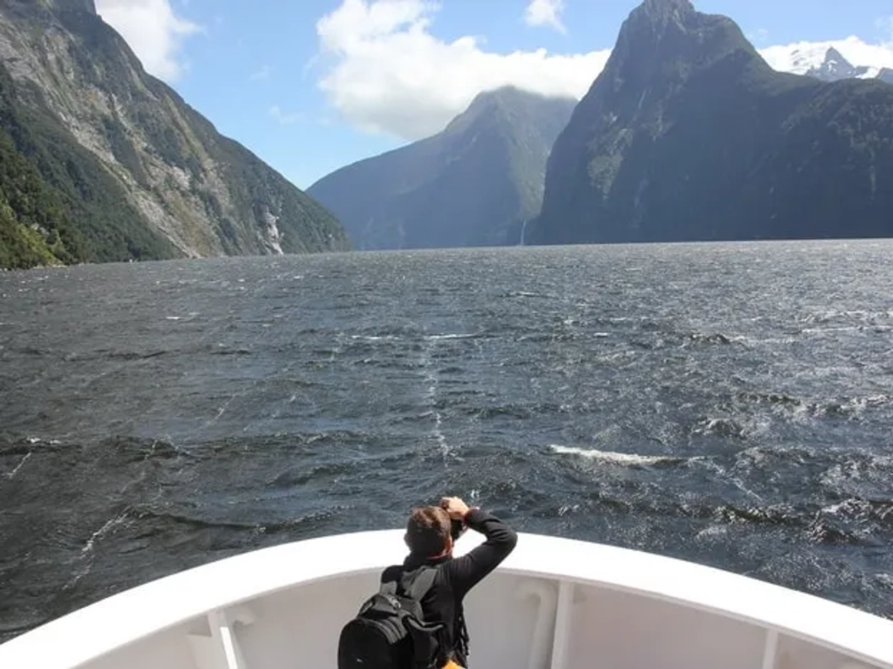 Persona en un barco observando paisajes montañosos y un mar agitado.