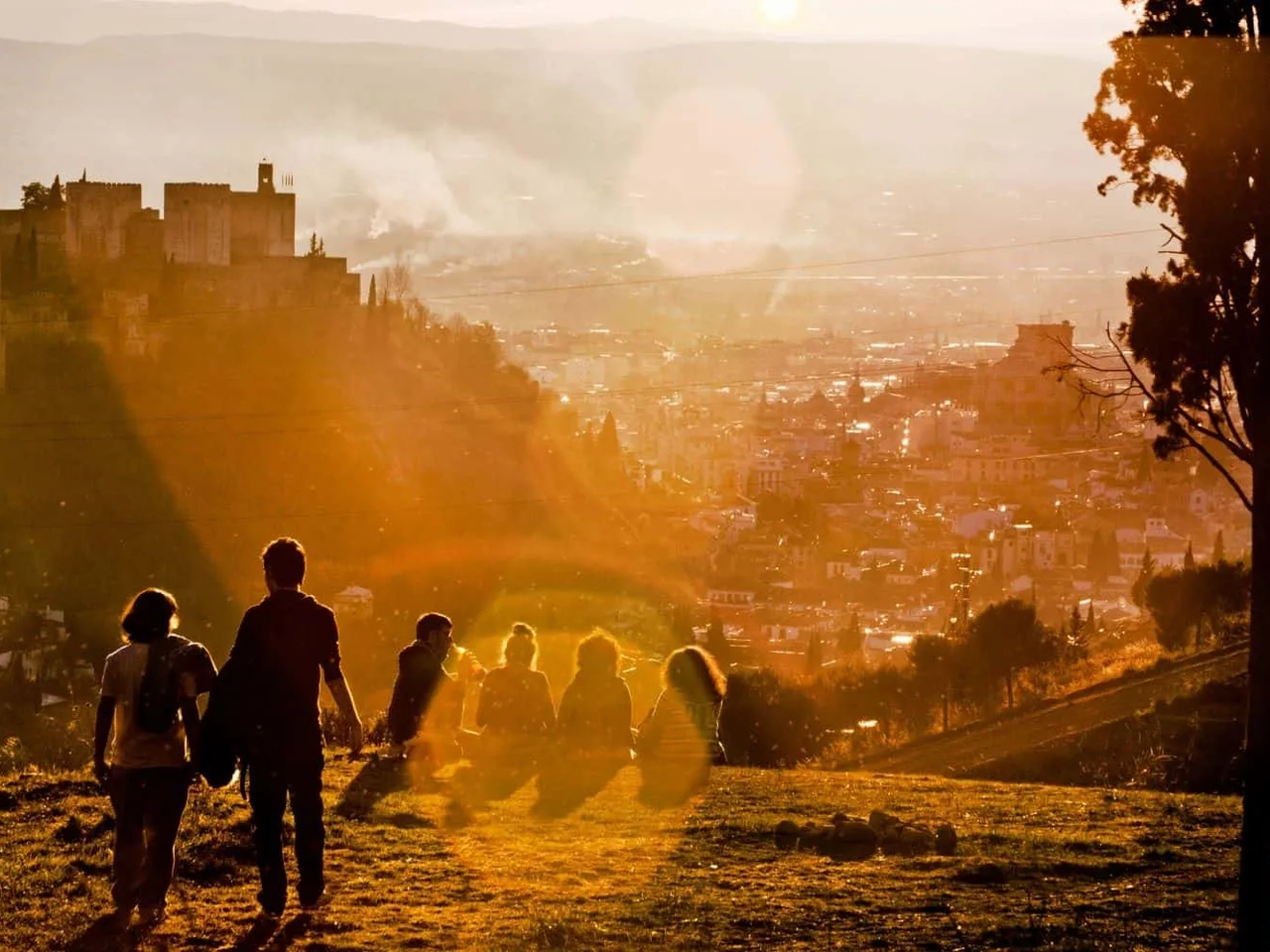 Grupo de pessoas apreciando o pôr do sol em uma colina com vista para a cidade.