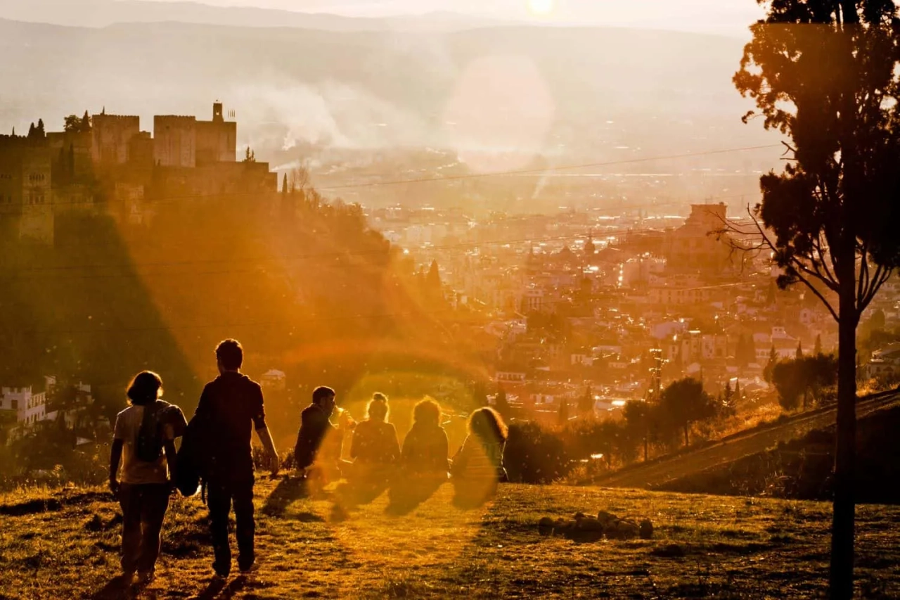 Grupo de pessoas apreciando o pôr do sol em uma colina com vista para a cidade.