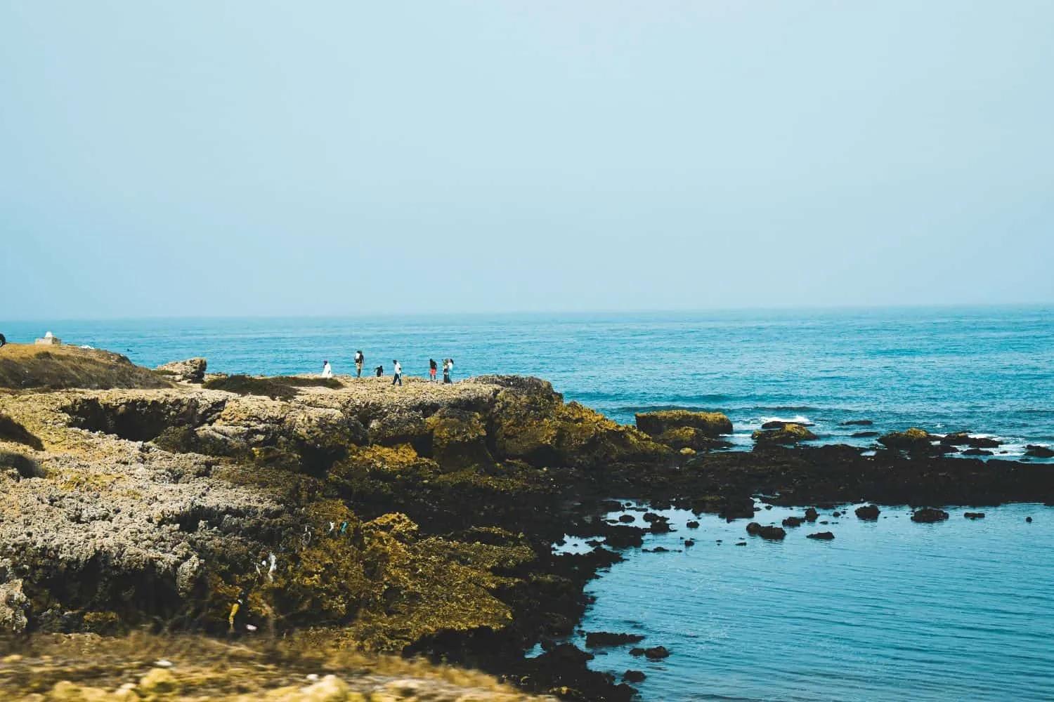 Pessoas caminhando em uma costa rochosa com vista para o mar em Marrocos.