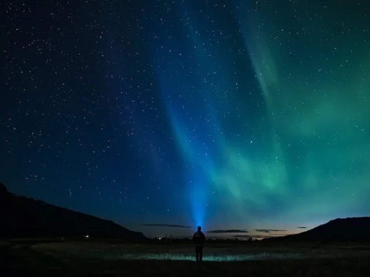 pessoa a ver auroras boreais na islândia azuis e verdes