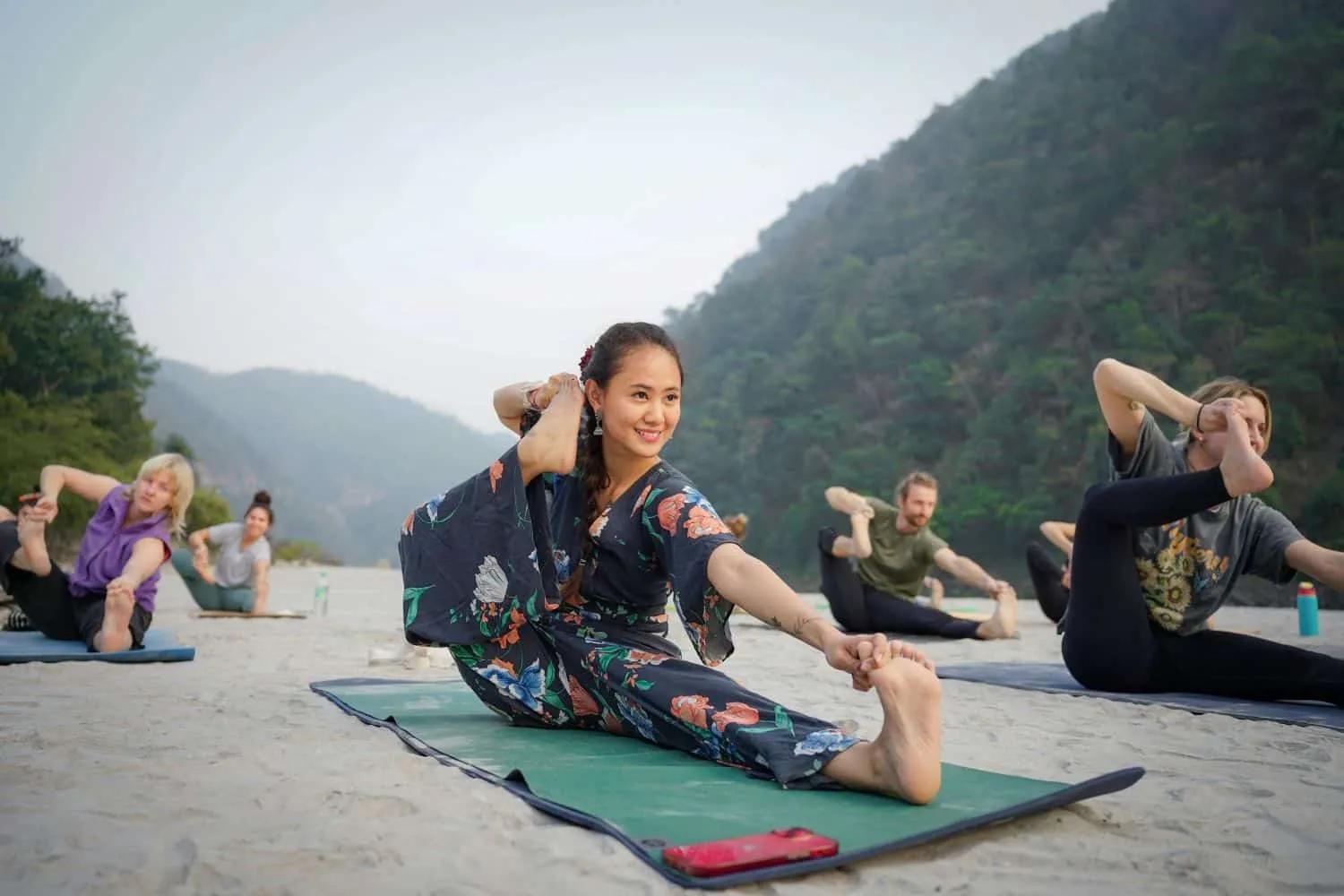 Grupo de pessoas praticando yoga em um ambiente natural, com montanhas ao fundo.