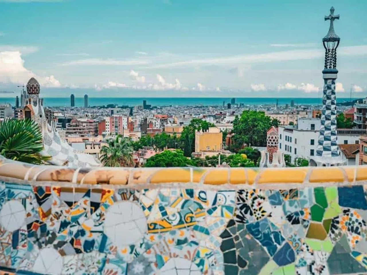 Vista panorámica de Barcelona desde el Parque Güell, con mosaicos coloridos y mar.