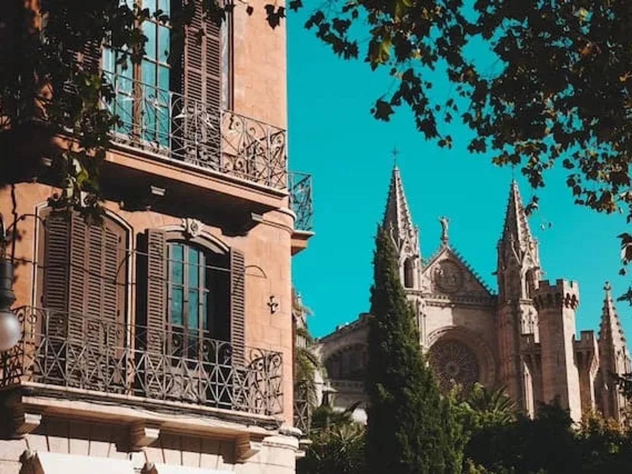Edifício histórico com janelas de ferro e catedral ao fundo em dia ensolarado.