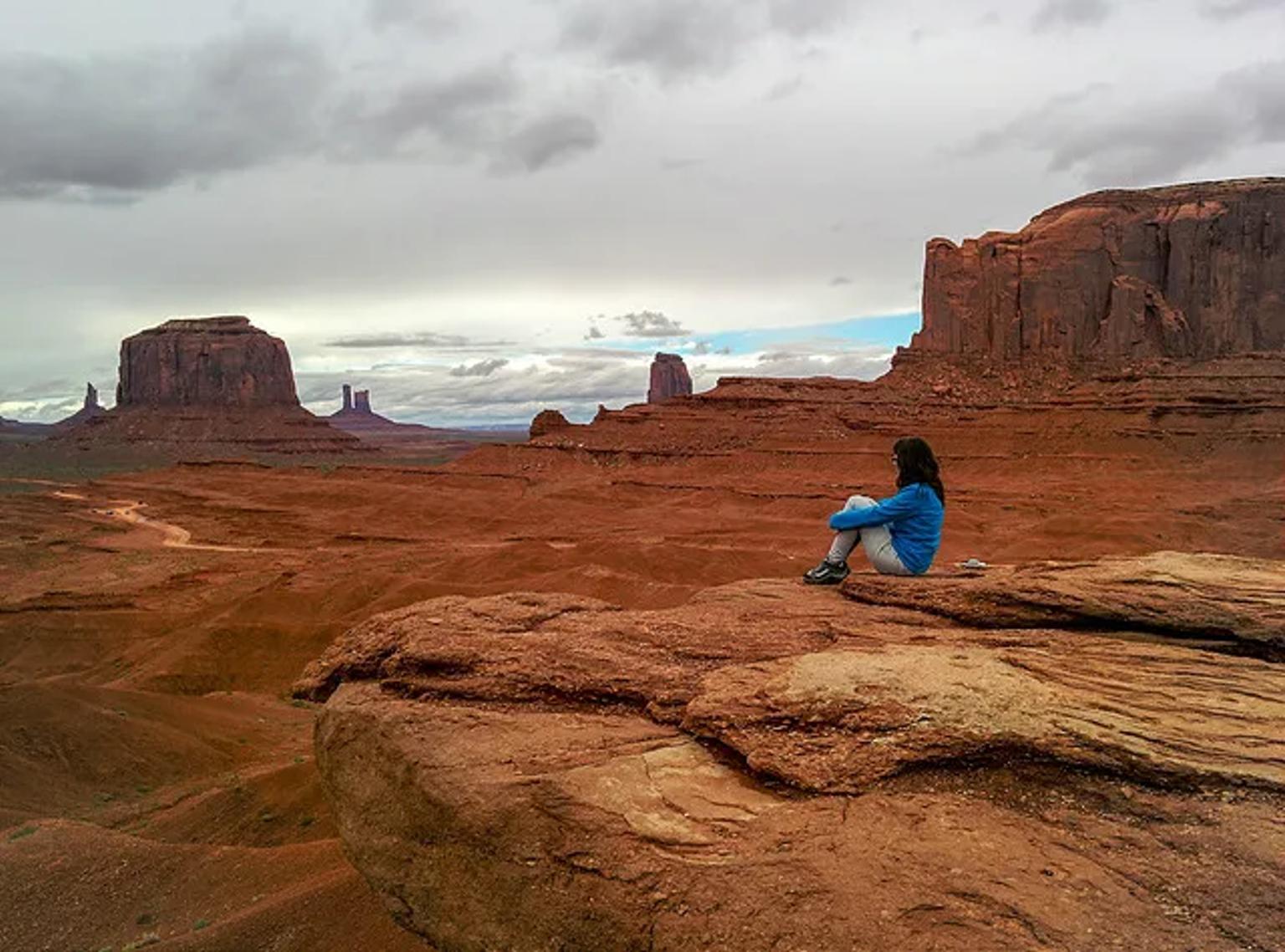 Mujer sentada en una roca, contemplando un paisaje desértico con formaciones rocosas.