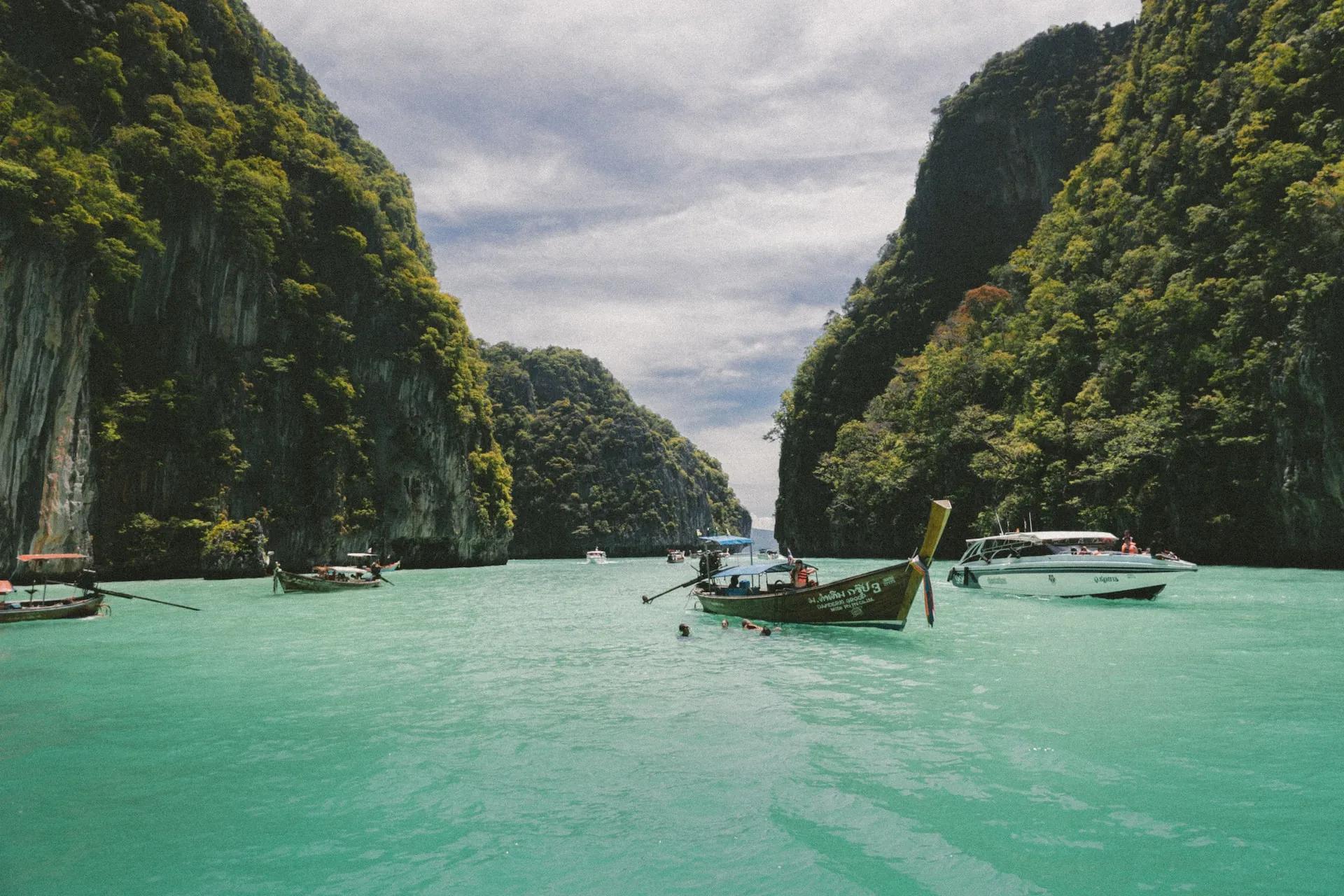 Turquoise waters surrounded by lush cliffs and boats in a scenic bay.