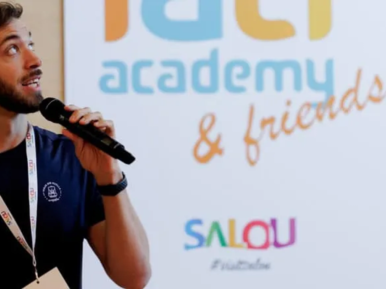 Hombre hablando con micrófono frente a un cartel de IATI Academy & Friends.