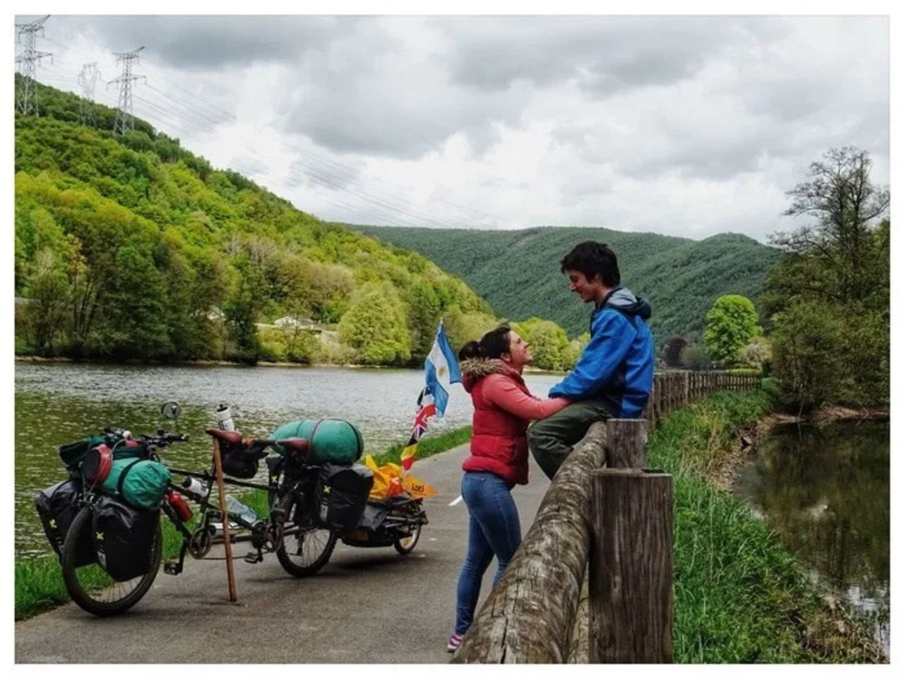 Pareja sonriente junto a bicicletas en un paisaje natural junto al agua.