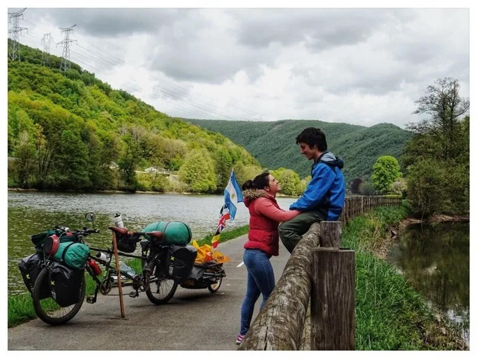 Pareja sonriente junto a bicicletas en un paisaje natural junto al río.