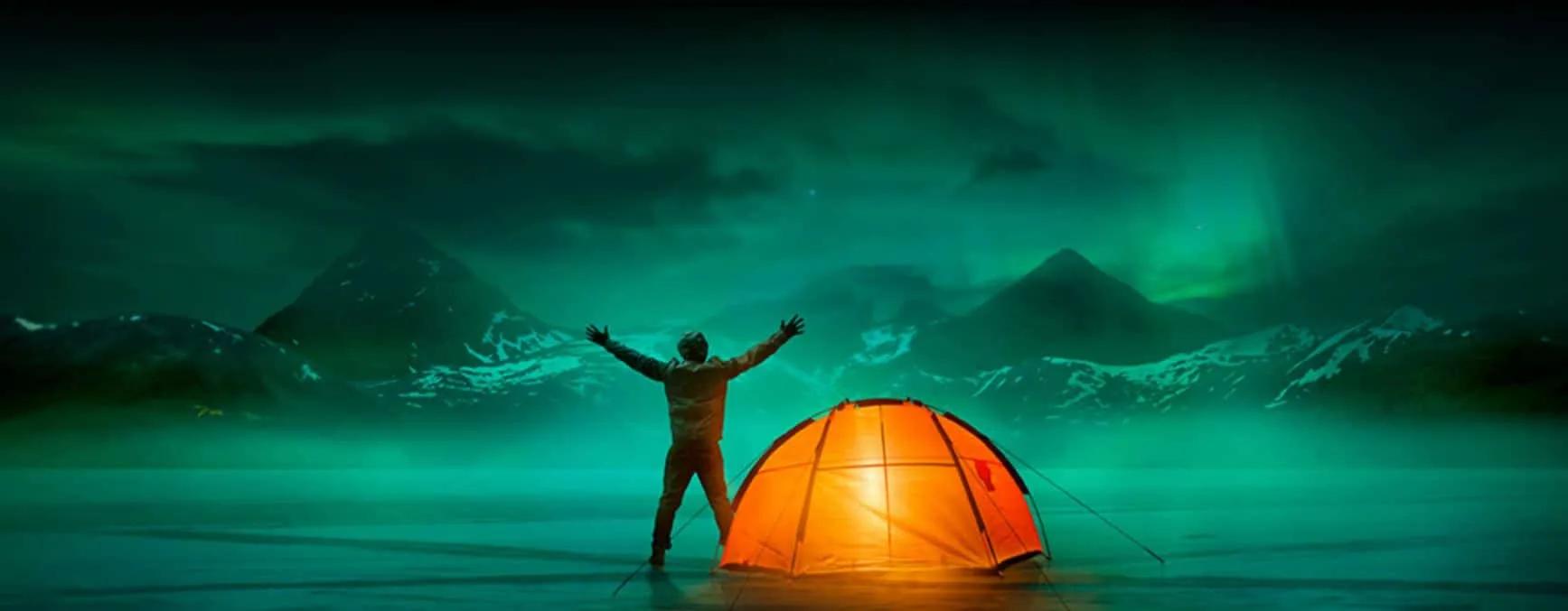 rapaz com tenda laranja ve as auroras boreais