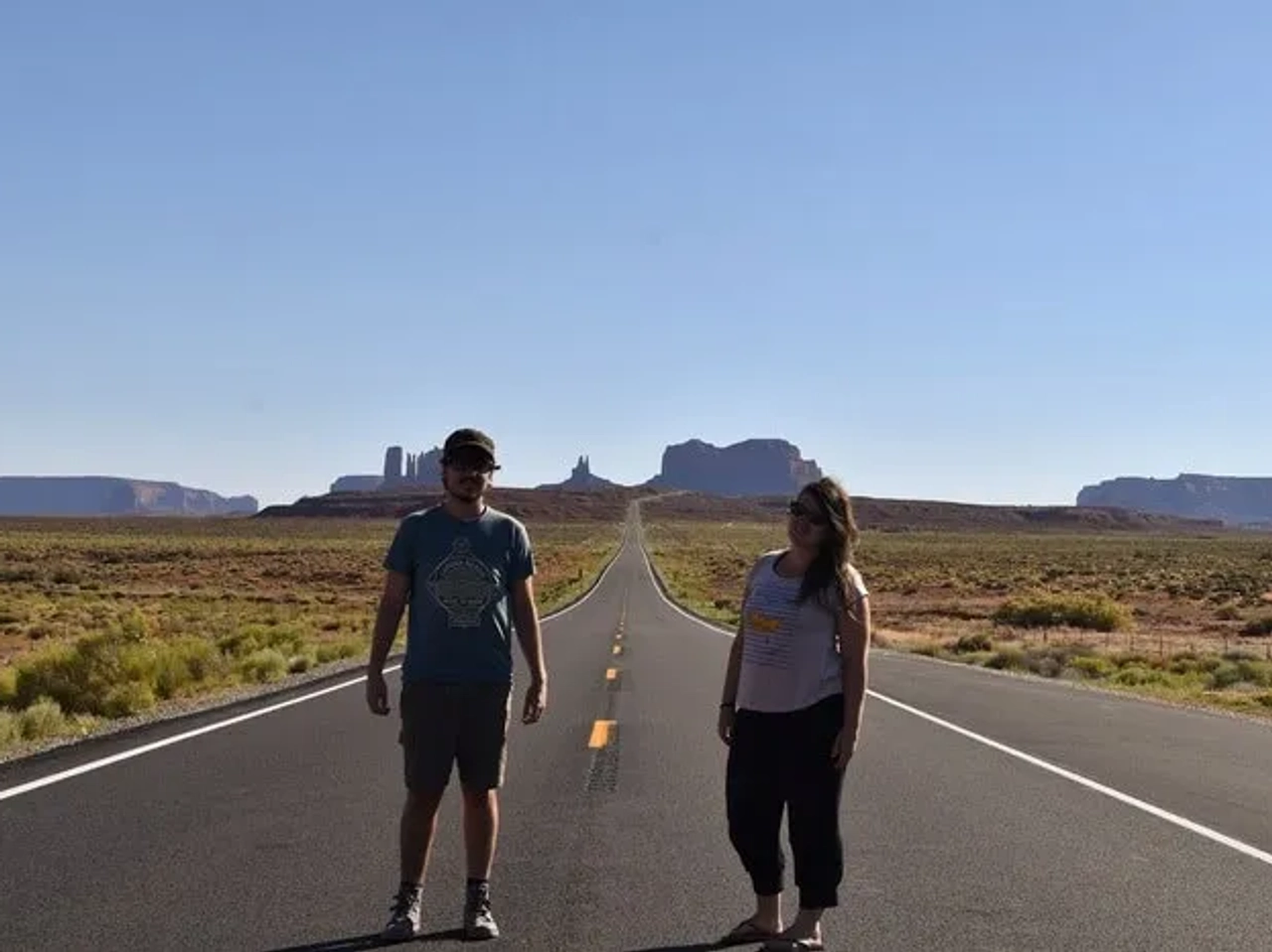 Pareja de viajeros en una carretera desierta con paisajes áridos de fondo.